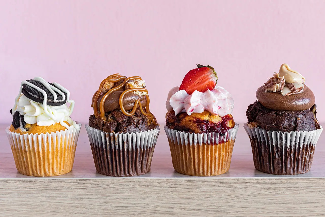 Τέσσερα cupcakes με γλάσο στη σειρά μπροστά σε ροζ τοίχο