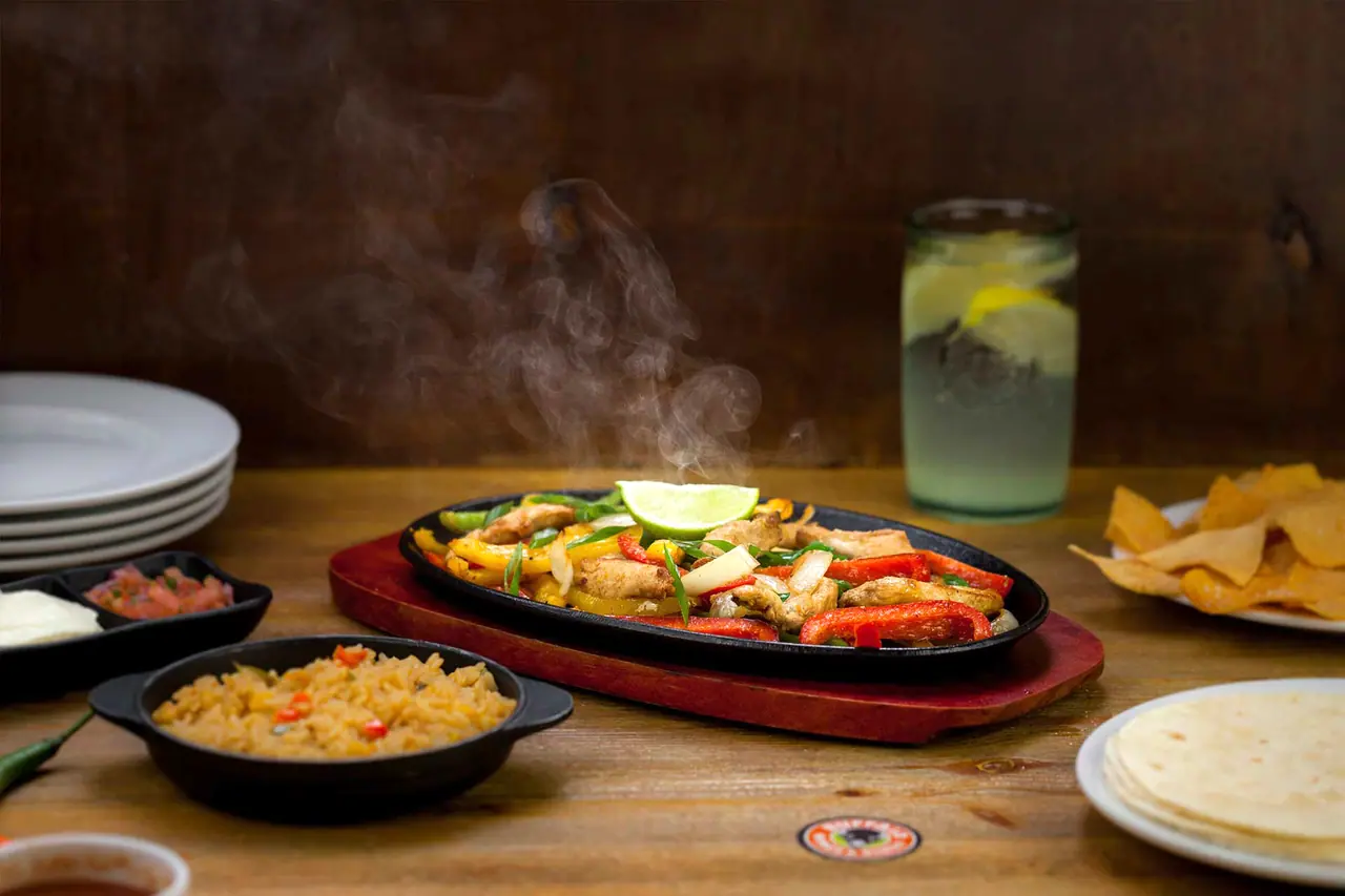 Αχνιστά fajitas κοτόπουλου σε καυτό τηγάνι με ρύζι, τορτίγιες και λεμονάδα
