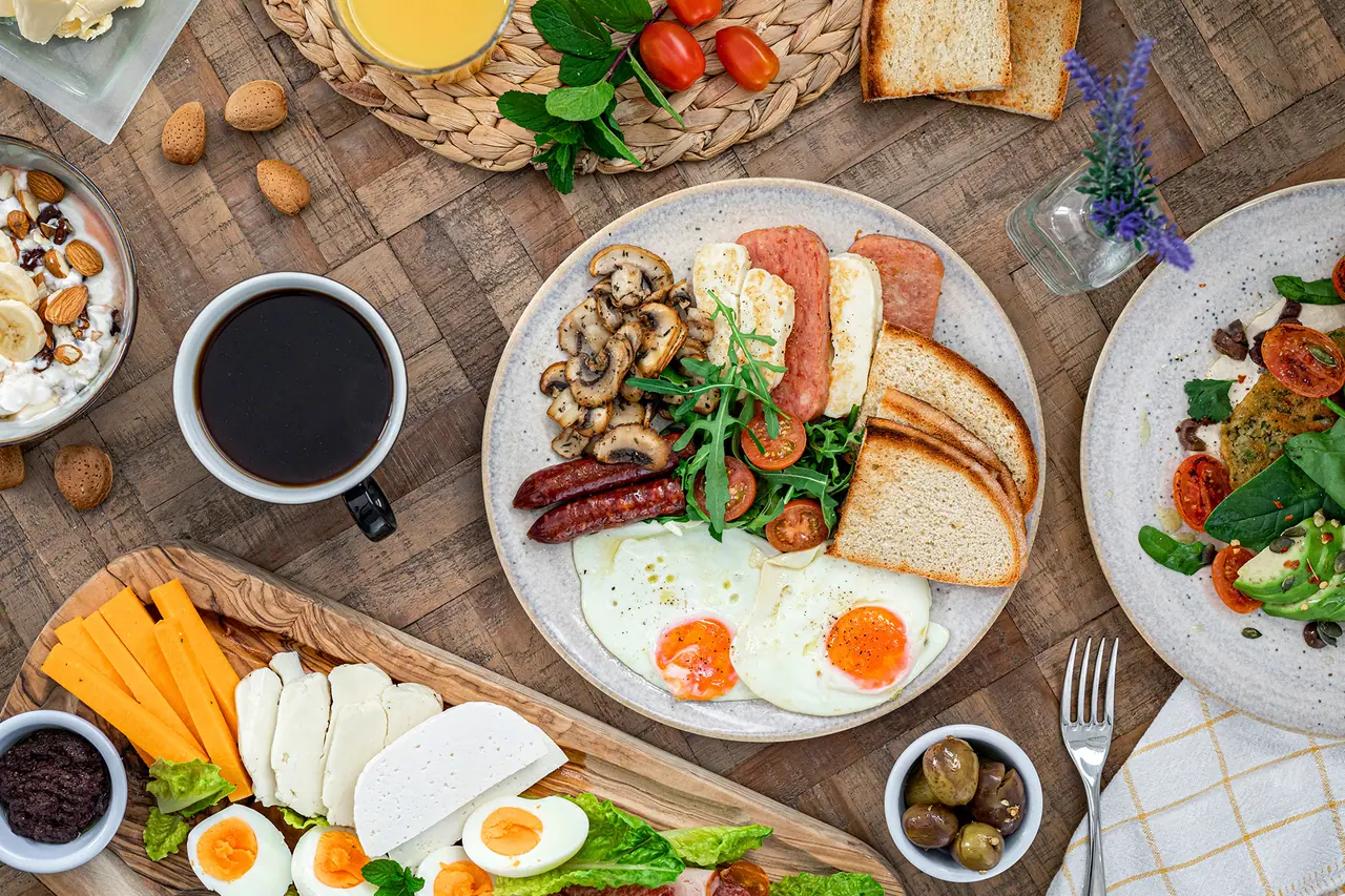 Κάτοψη τραπεζιού brunch με αυγά, λουκάνικα, χαλλούμι, ψωμί, καφέ και τυριά
